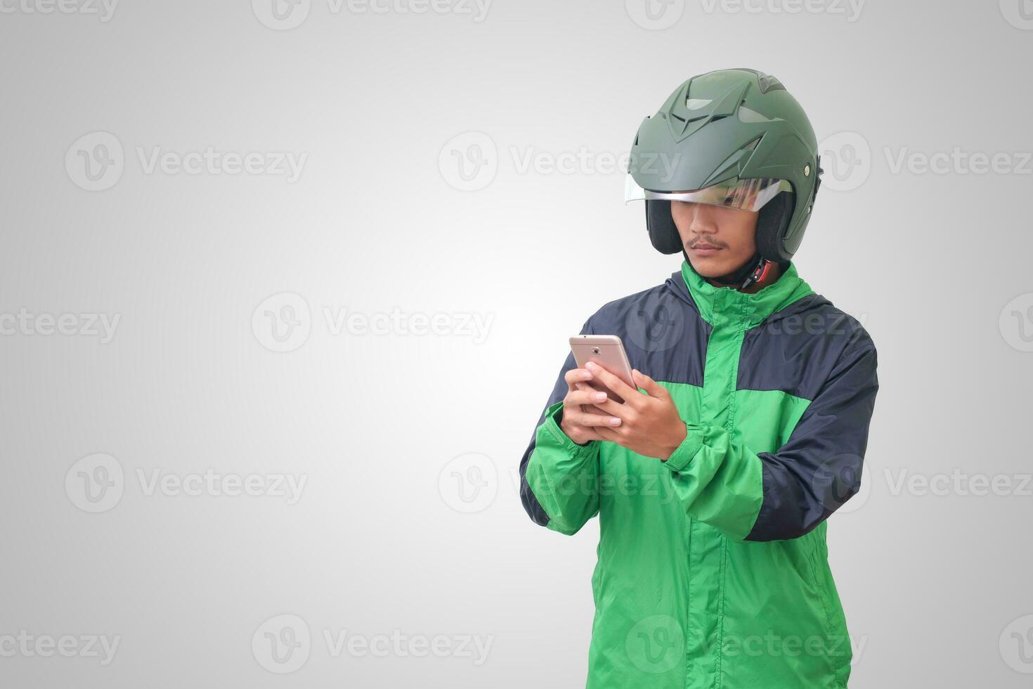 Portrait of Asian online taxi driver wearing green jacket and helmet holding a mobile phone and smiling. Advertising concept. Isolated image on white background photo