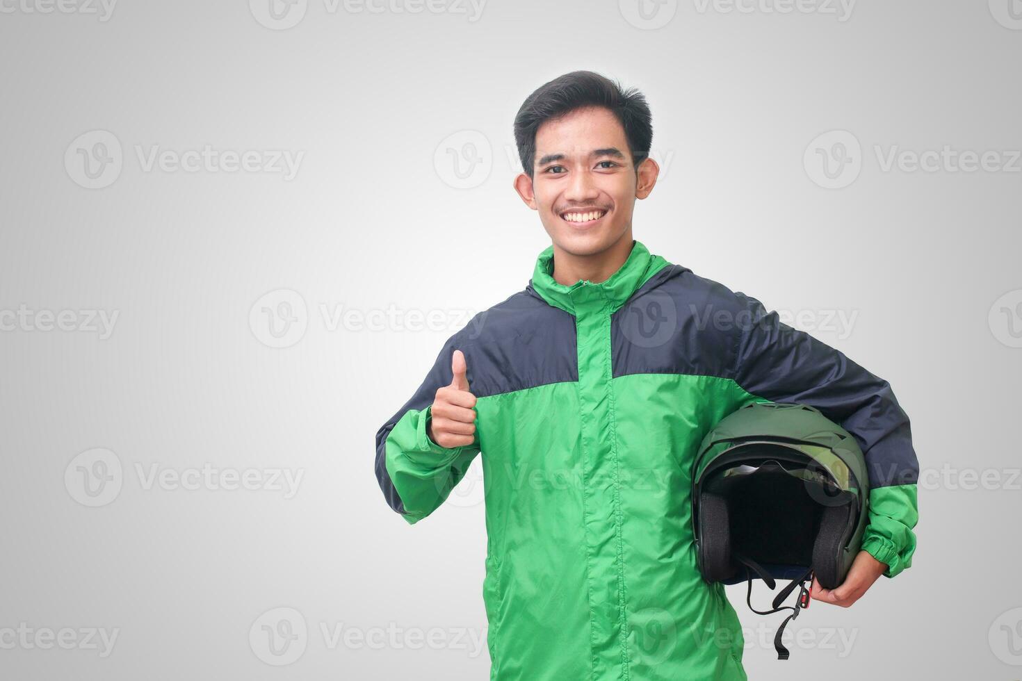 Portrait of Asian online taxi driver wearing green jacket and helmet showing good job sign, thumb up. Isolated image on white background photo