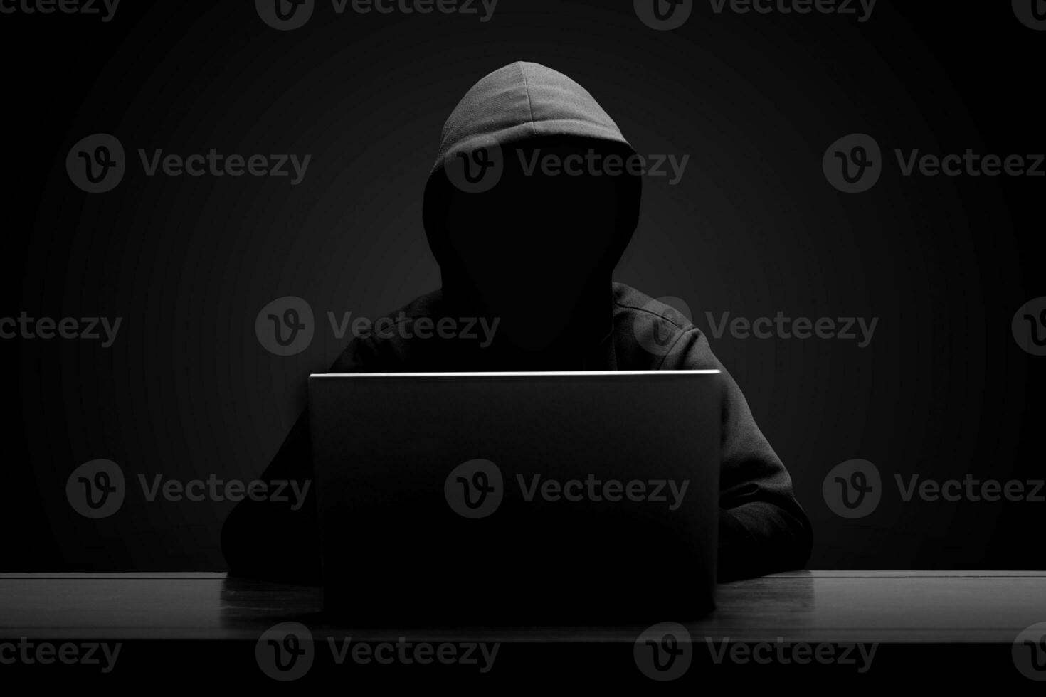 Mysterious man wearing black hoodie using laptop in the dark room. Hacker and cyber security concept. photo