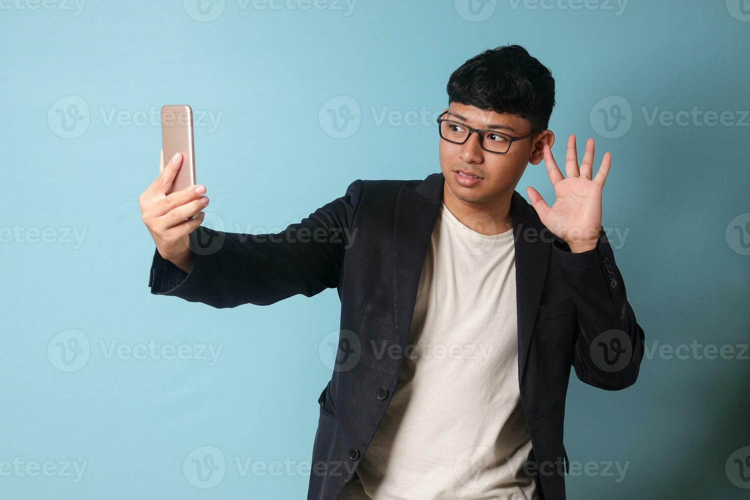 Portrait of young Asian business man in casual suit taking a selfie with confident and happy expression. Isolated image on blue background photo