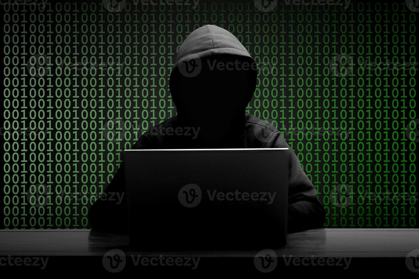 Mysterious man wearing black hoodie using laptop in the dark room. Hacker and cyber security concept. photo