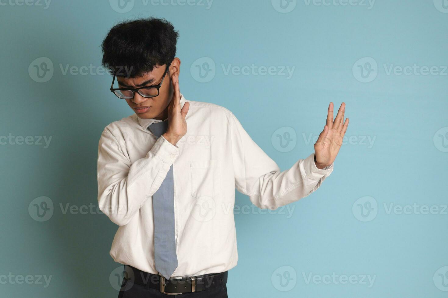 Indonesian senior high school student wearing white shirt uniform with gray tie forming a hand gesture to avoid something. Isolated image on blue background photo