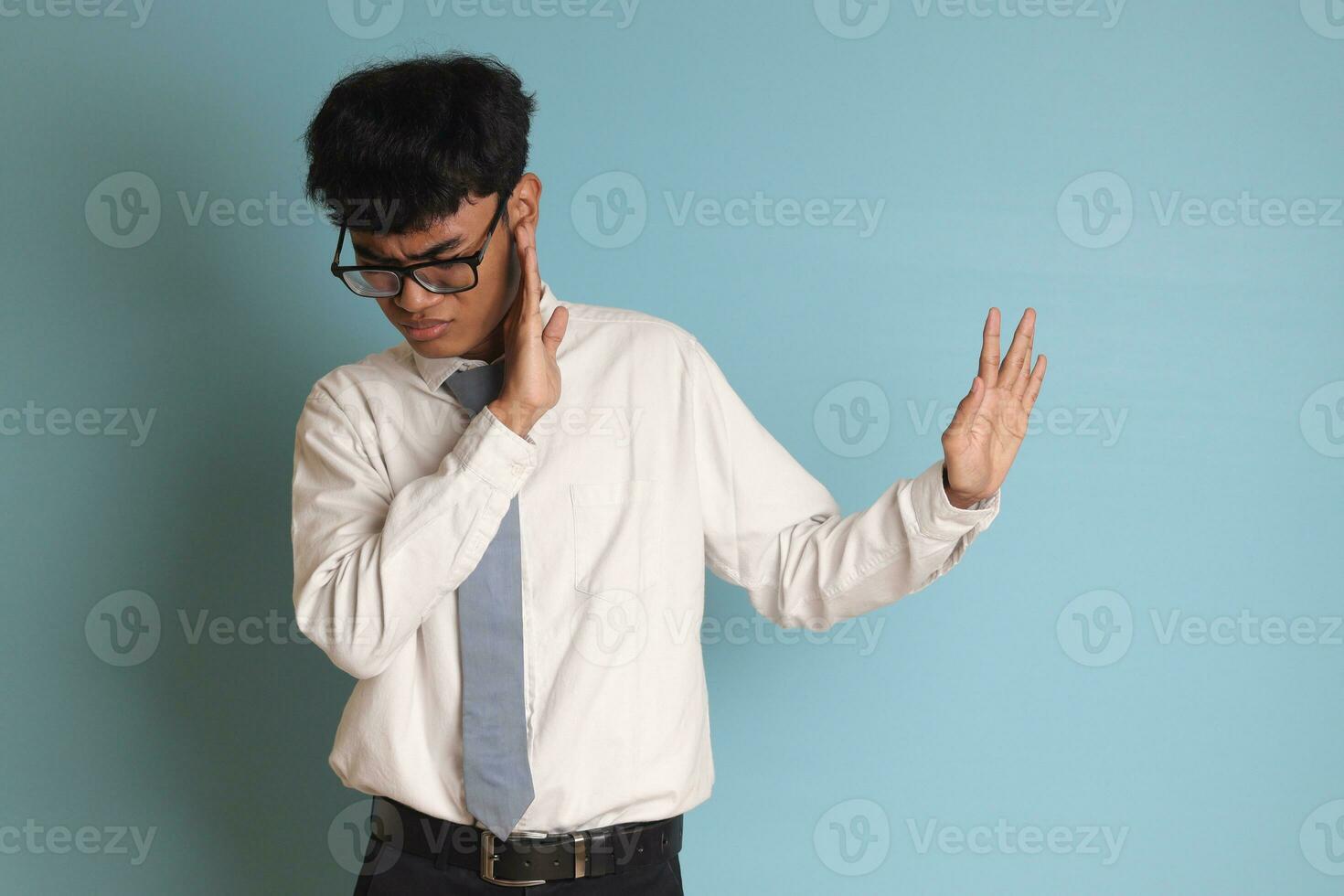 indonesio mayor alto colegio estudiante vistiendo blanco camisa uniforme con gris Corbata formando un mano gesto a evitar algo. aislado imagen en azul antecedentes foto