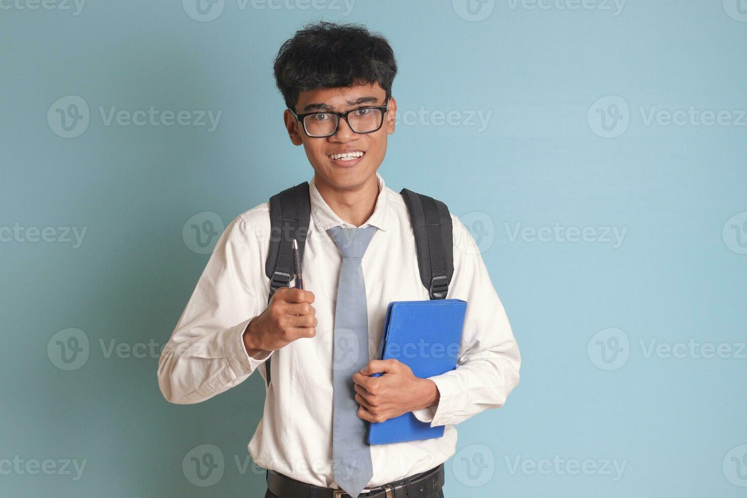 Indonesian senior high school student wearing white shirt uniform with gray tie writing on note book using pen. Isolated image on blue background photo