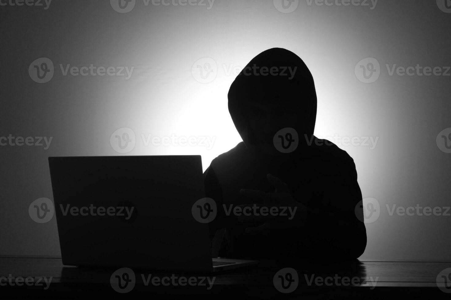 Mysterious man wearing black hoodie using laptop and holding credit card in the dark room. Hacker and cyber security concept. photo