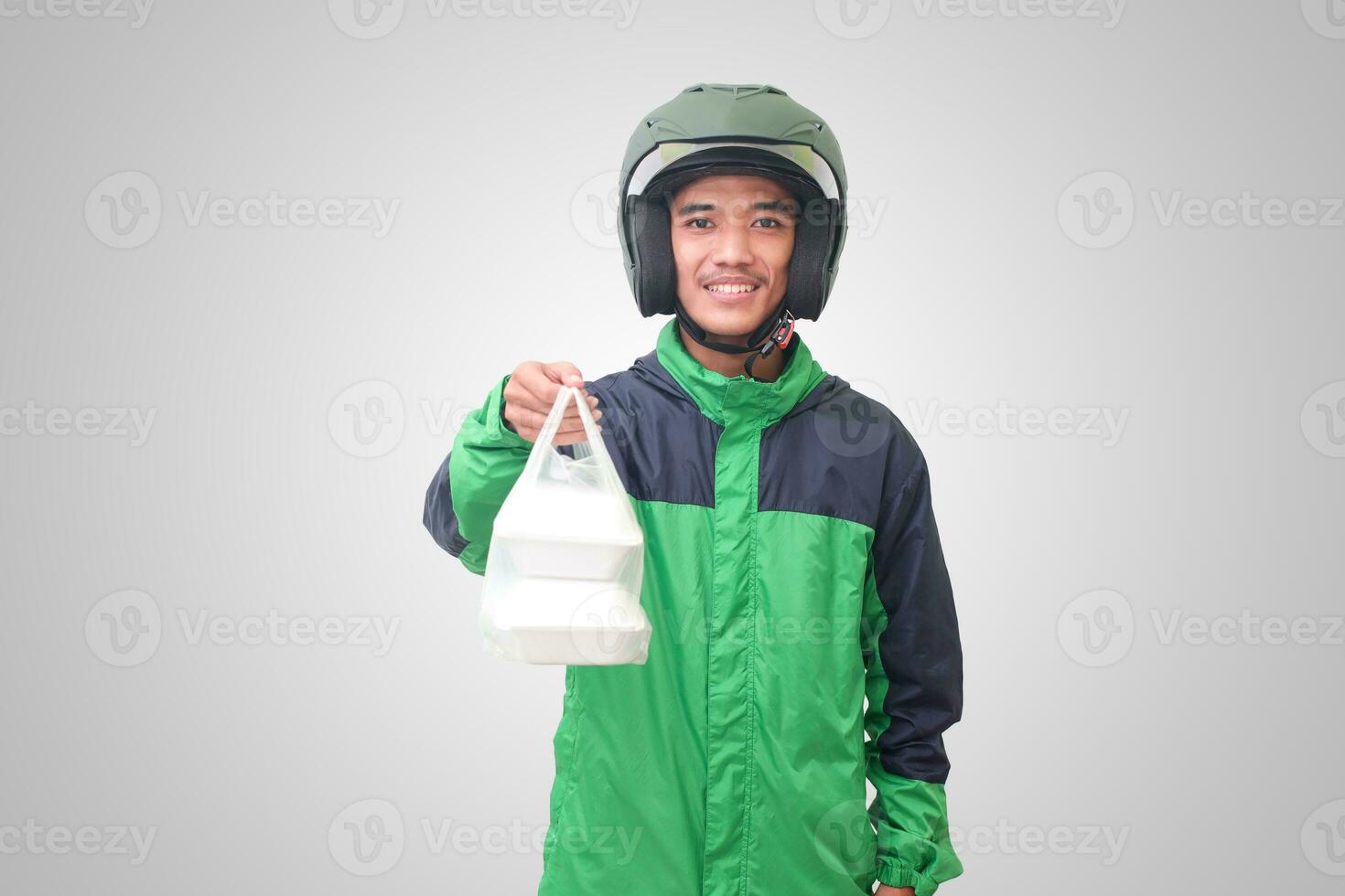 Portrait of Asian online taxi driver wearing green jacket and helmet holding food wrapped in foam plastic box. Isolated image on white background photo