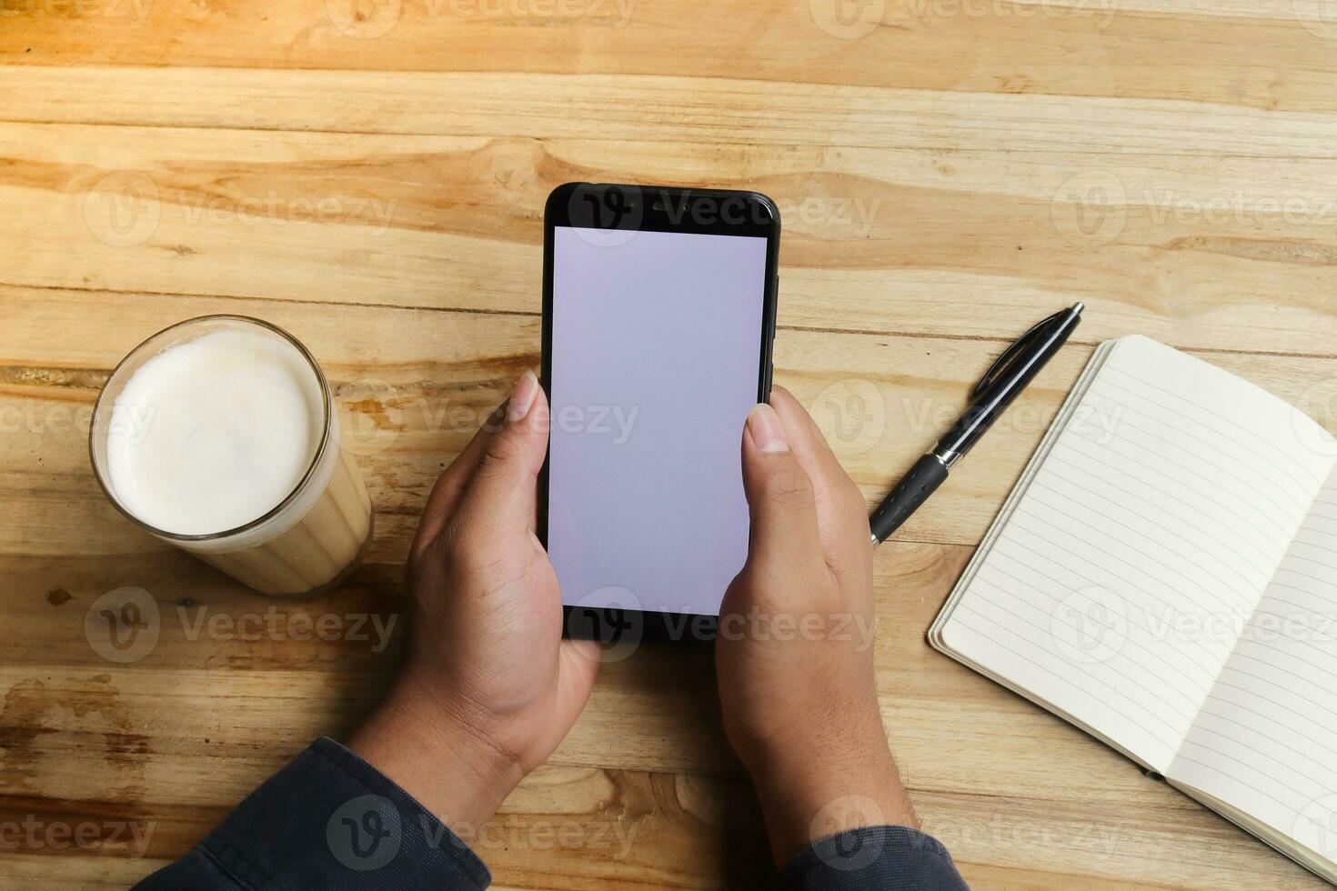 cerca arriba de masculino mano utilizando móvil teléfono en blanco pantalla con vacío cuaderno y un taza de café mientras sentado a café foto