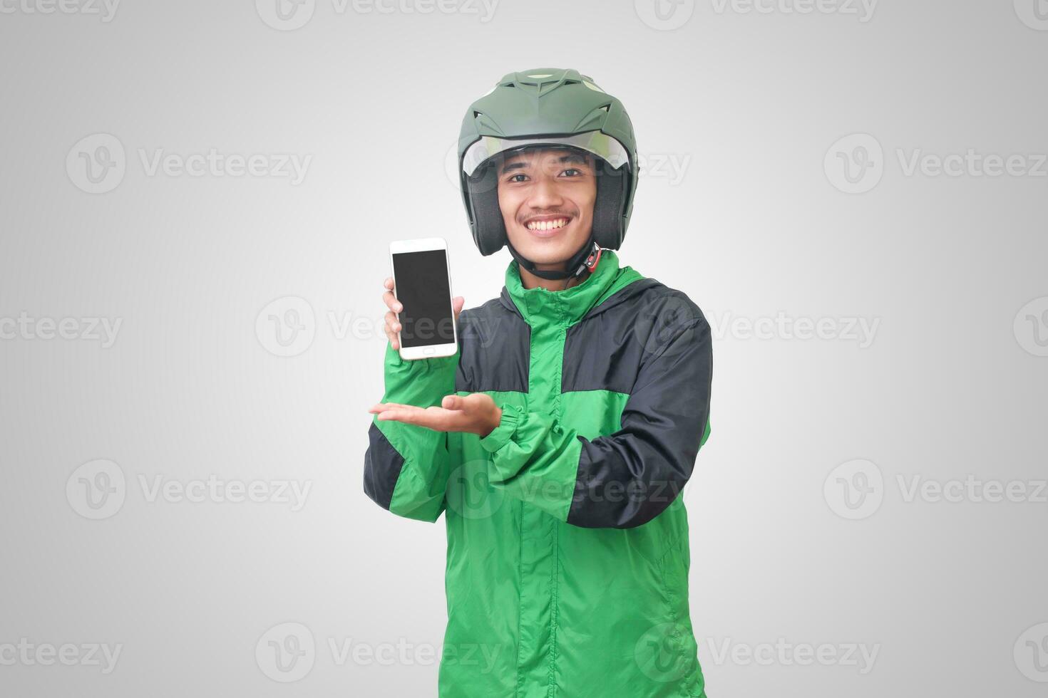 Portrait of Asian online taxi driver wearing green jacket and helmet showing and presenting blank screen mobile phone. Isolated image on white background photo