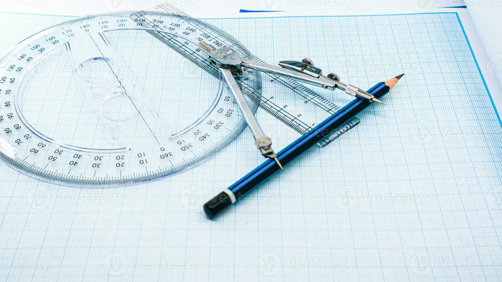 On blue graph paper are compasses, protractor, ruler, and a pencil photo