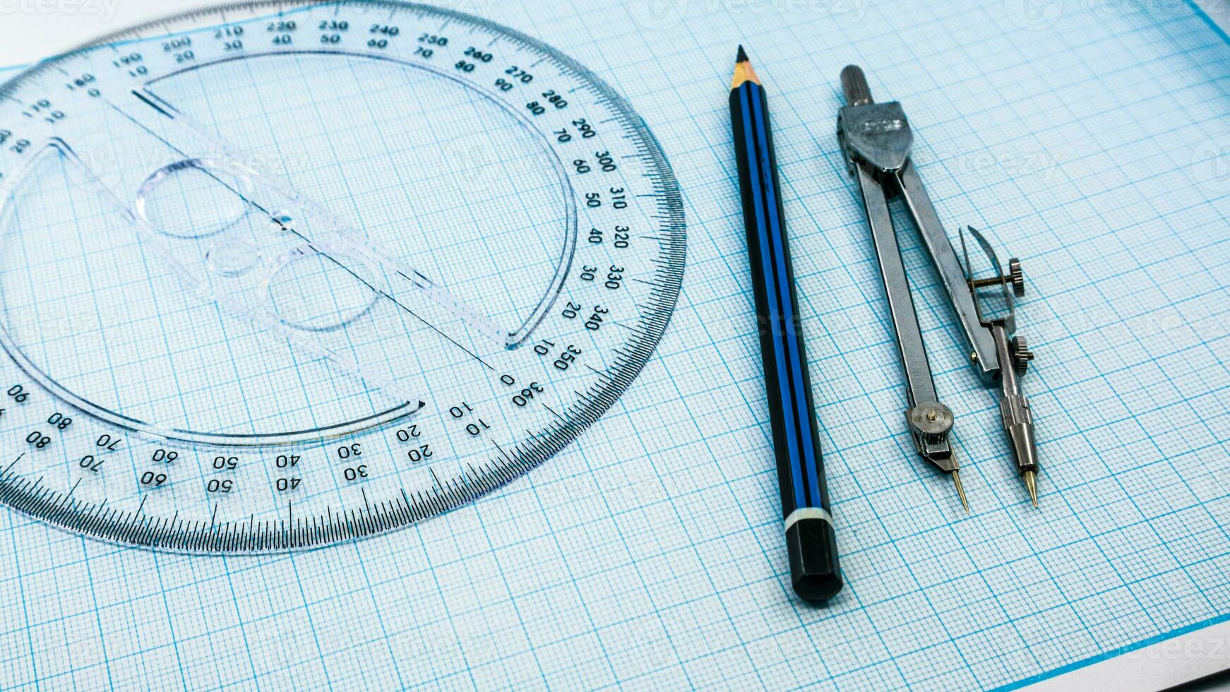 On blue graph paper are compasses, protractor, ruler, and a pencil photo