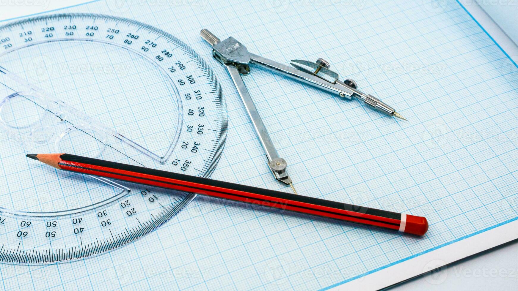 On blue graph paper are compasses, protractor, ruler, and a pencil photo