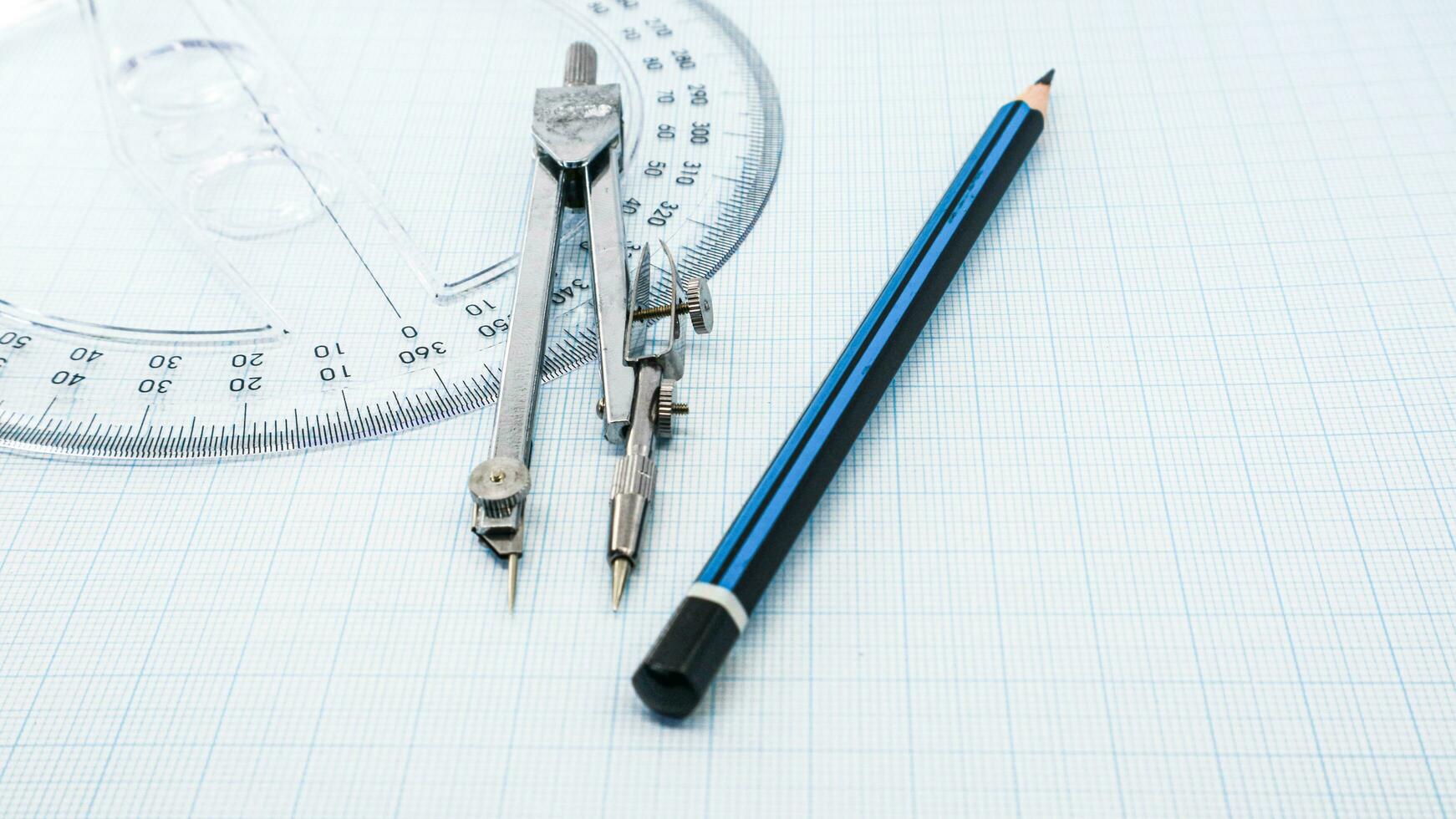 On blue graph paper are compasses, protractor, ruler, and a pencil photo