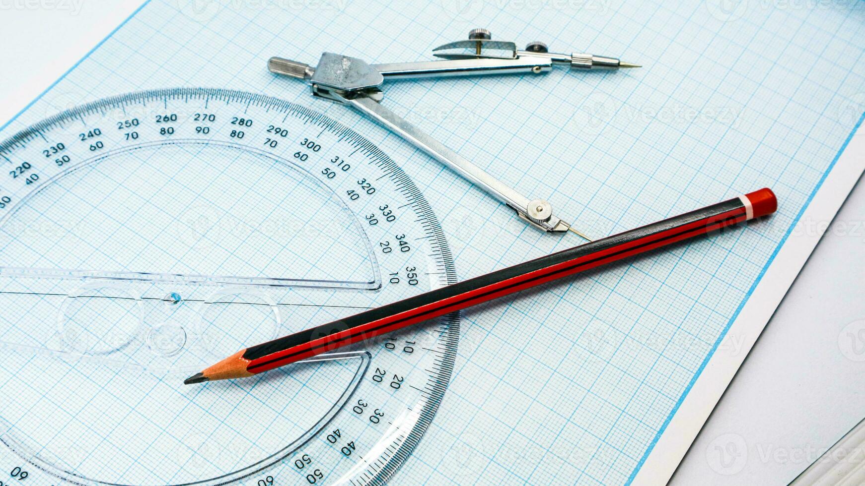 On blue graph paper are compasses, protractor, ruler, and a pencil photo