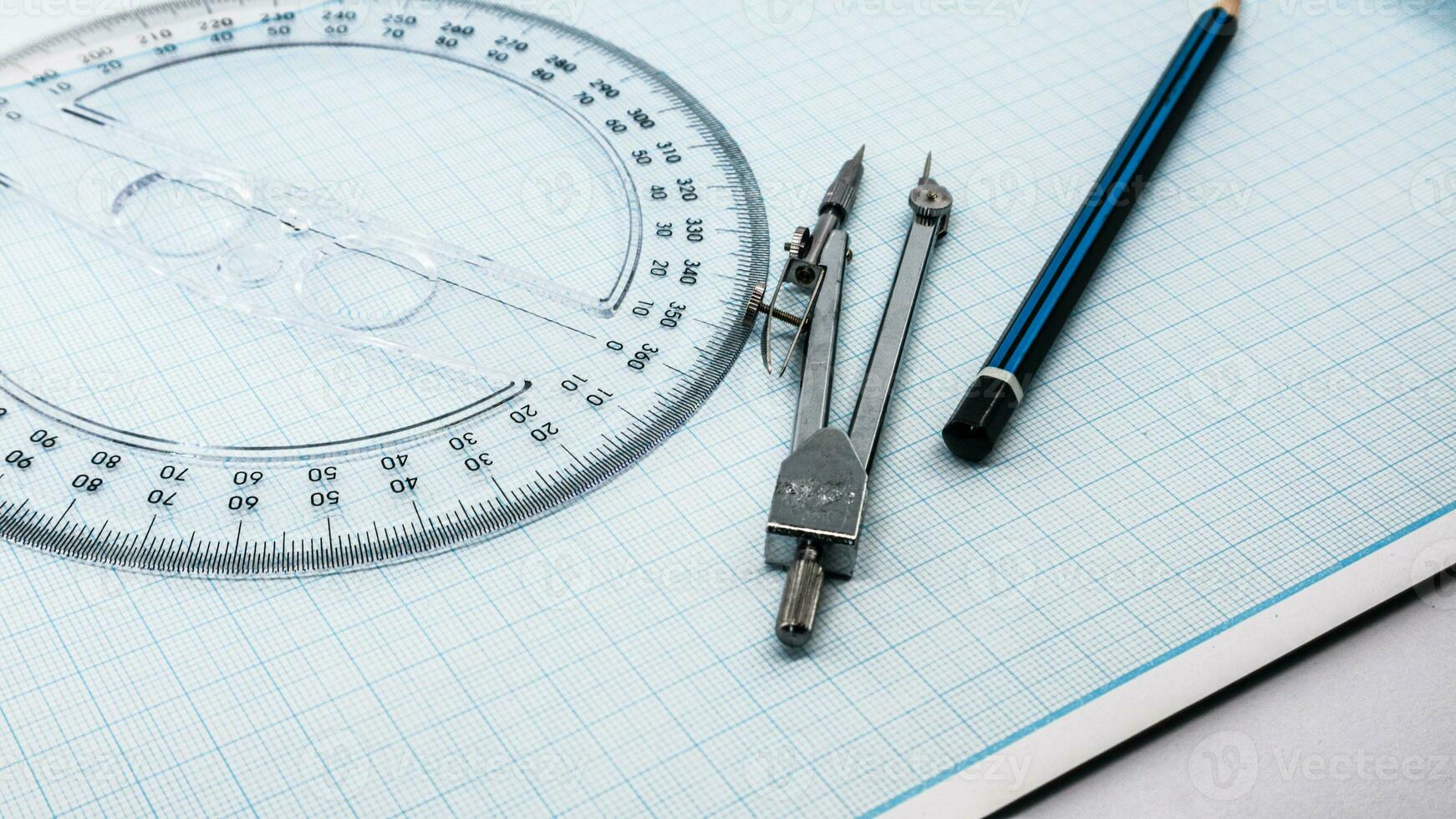 On blue graph paper are compasses, protractor, ruler, and a pencil photo