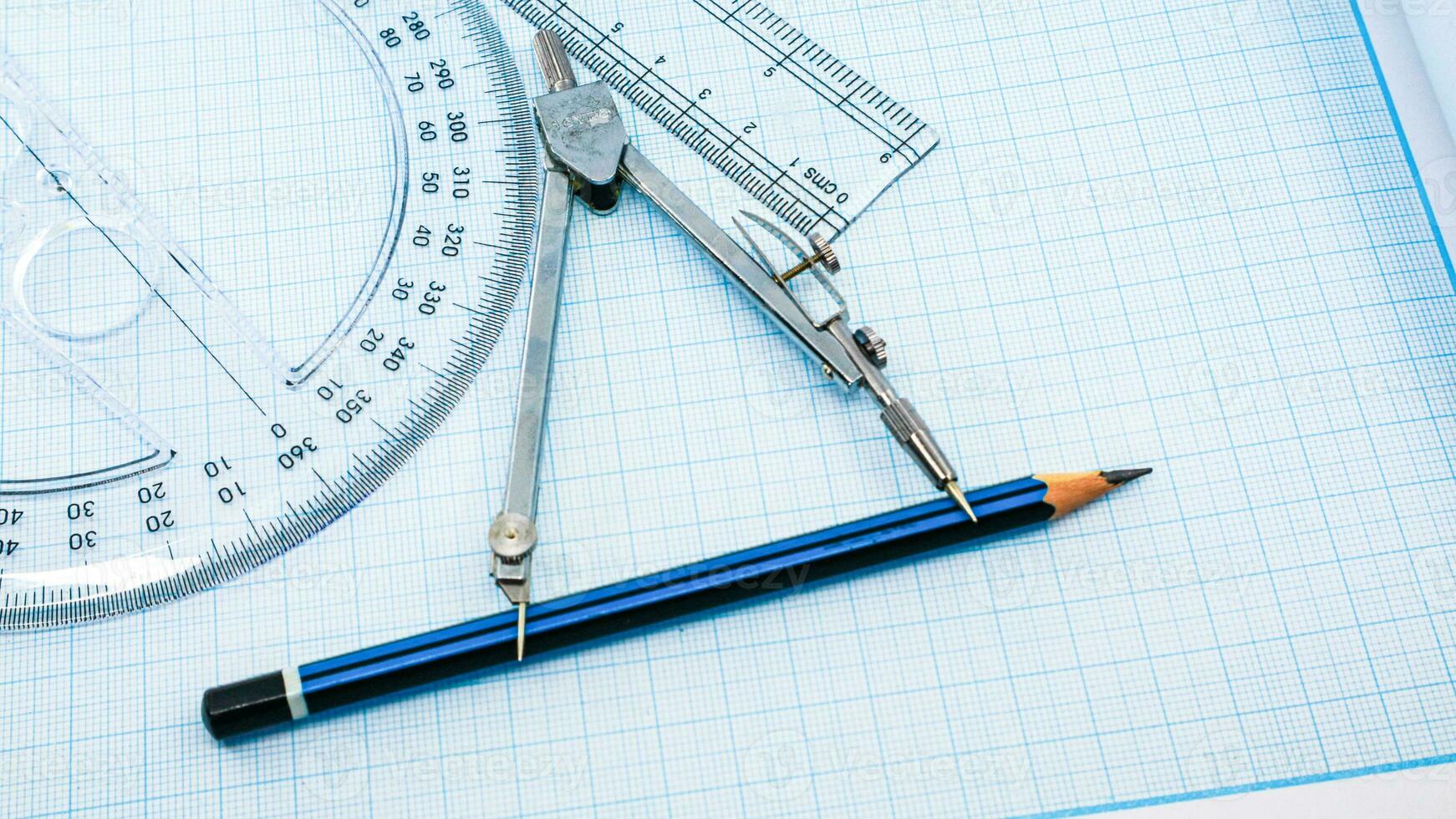 On blue graph paper are compasses, protractor, ruler, and a pencil photo