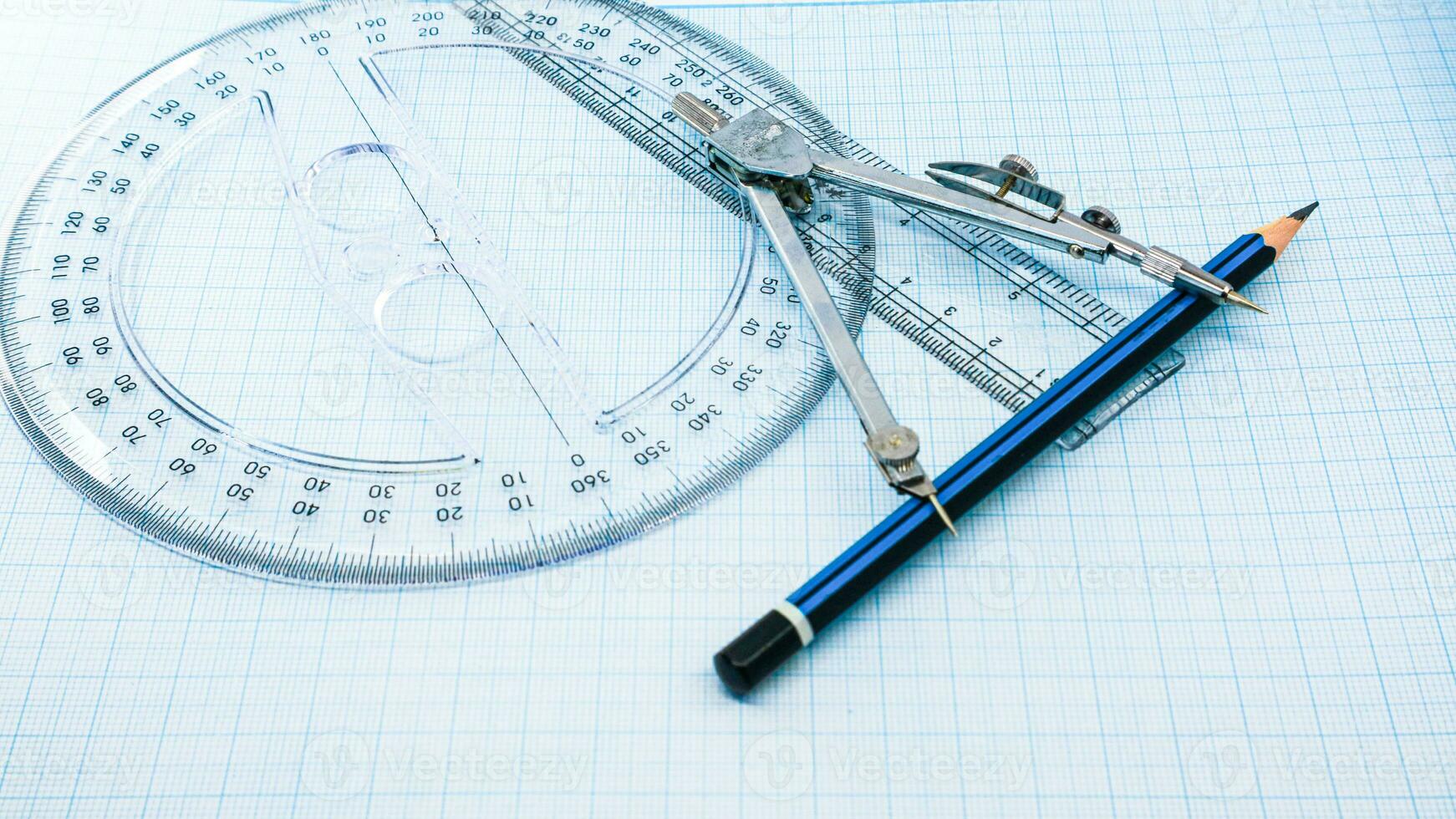 On blue graph paper are compasses, protractor, ruler, and a pencil photo