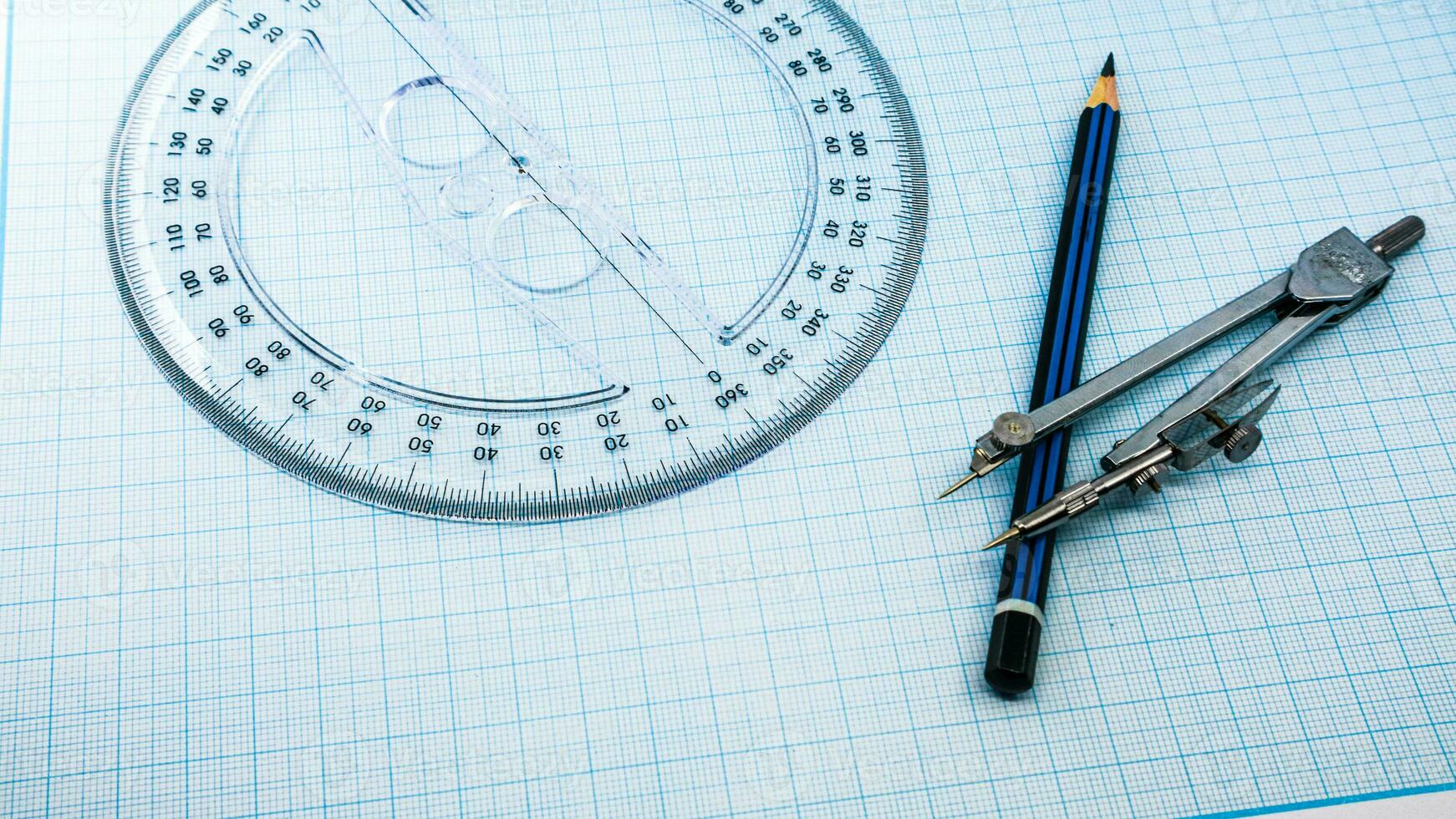 On blue graph paper are compasses, protractor, ruler, and a pencil photo