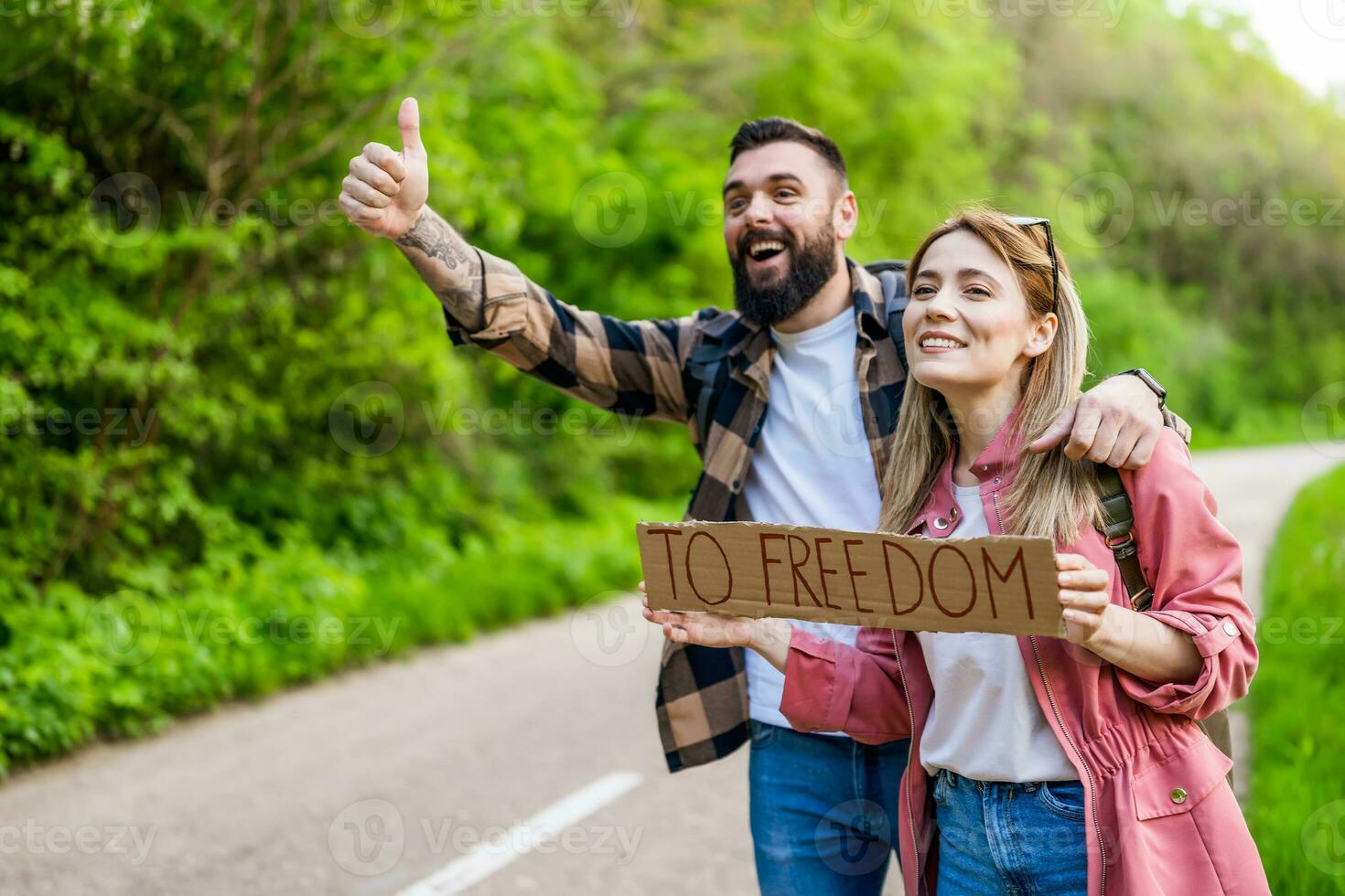 Happy couple hitchhiking on roadside trying to stop car. They are holding cardboard with inscription. photo