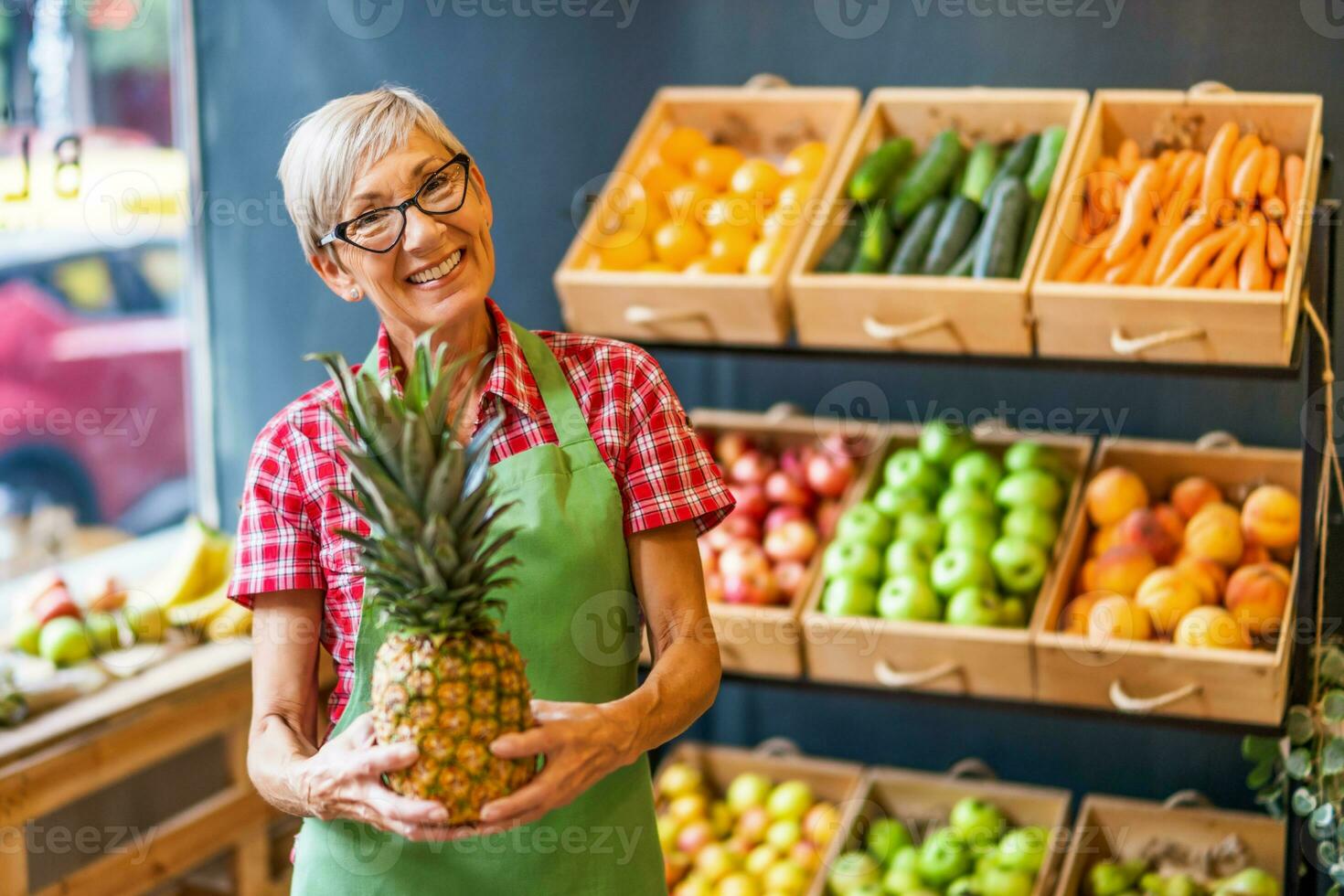 Mature woman works in fruits and vegetables shop. She is holding pineapple. photo