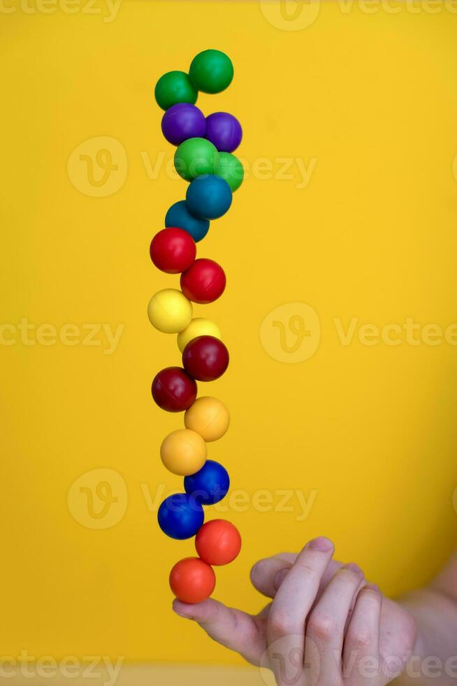 Balancing colored plastic balls on a finger on a yellow background. photo