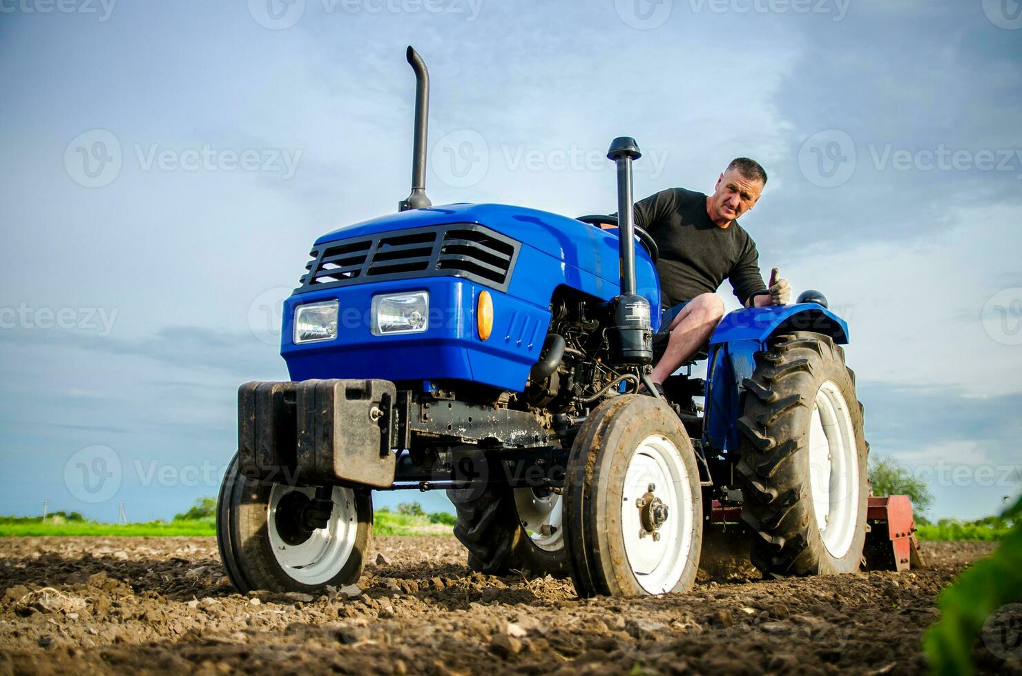 A farmer on a tractor cleans the field after harvest. Preparation of land for future planting new crop. Intensive land use. Milling soil, loosening ground before cutting rows. Farming, agriculture. photo