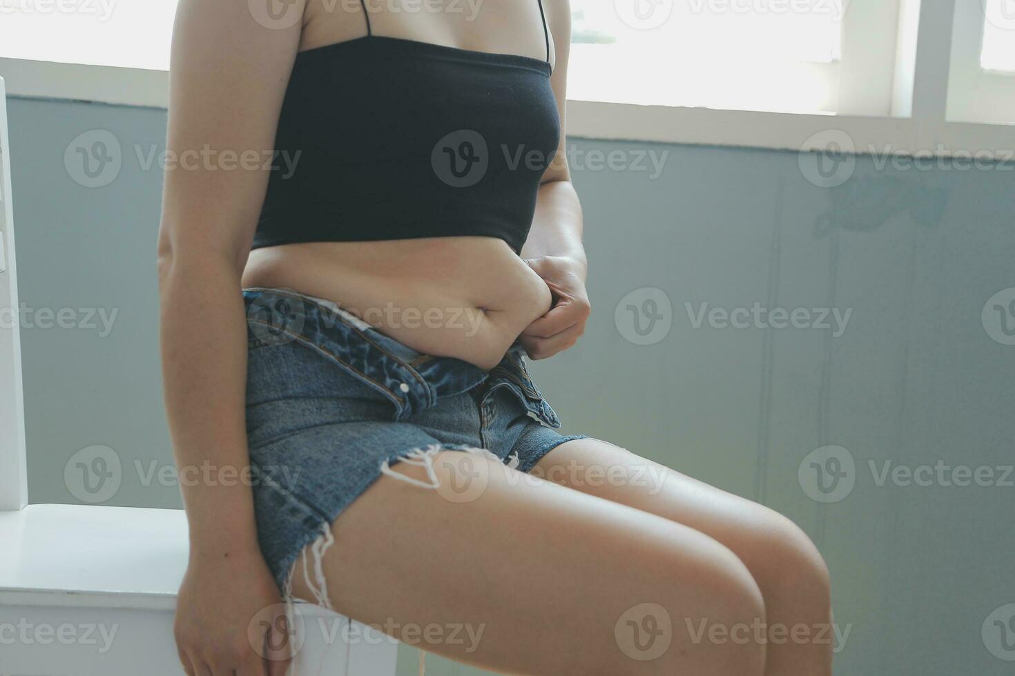 Close up of a belly with scar from c-section and abdominal fat. Women's health. A woman dressed up in sportswear demonstrating her imperfect body after a childbirth with nursery on the background. photo