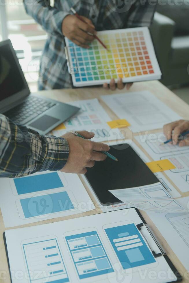 Close up ux developer and ui designer brainstorming about mobile app interface wireframe design on table with customer breif and color code at modern office.Creative digital development agency photo
