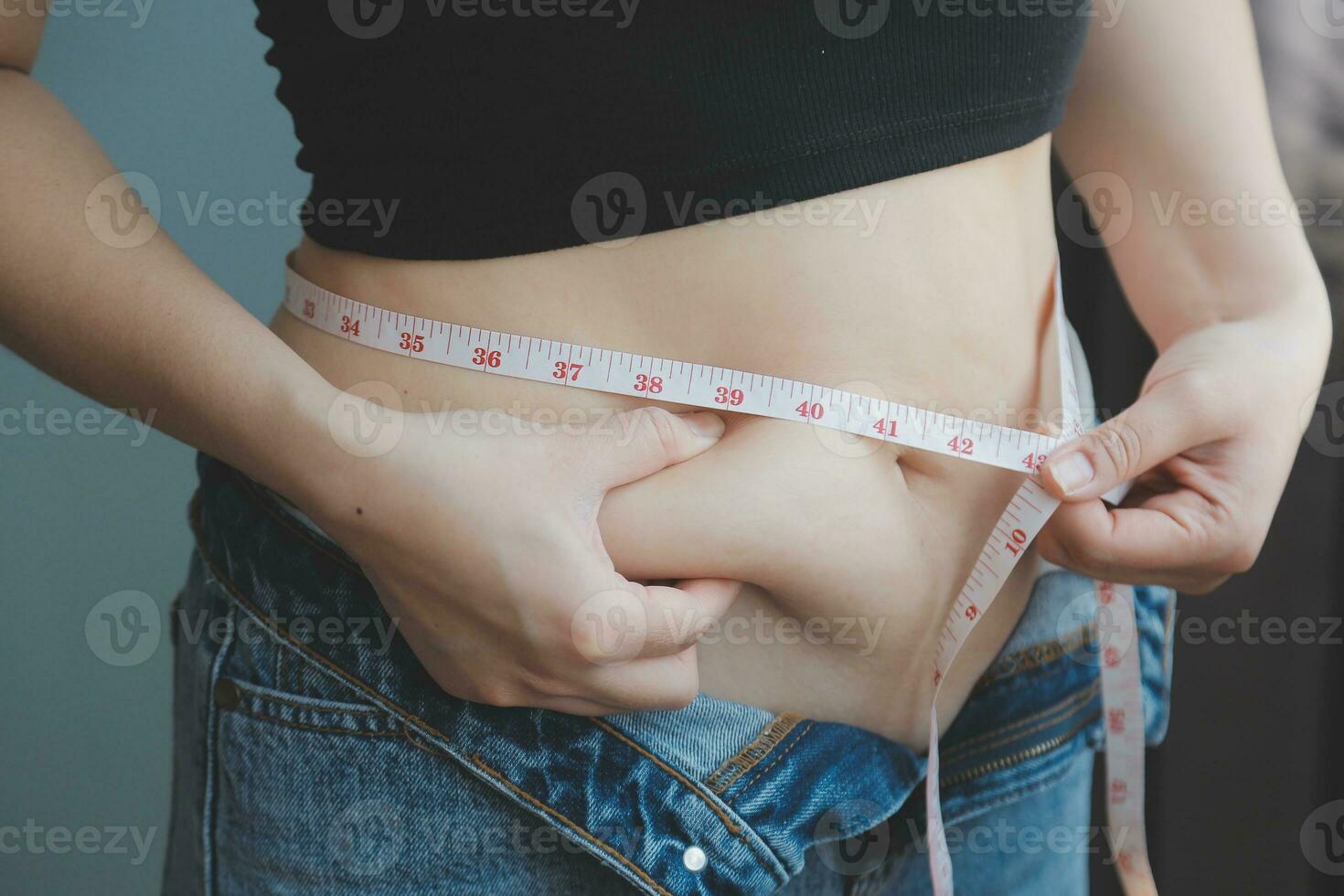 mujer gorda, barriga gorda, gordita, mujer obesa mano sosteniendo grasa abdominal excesiva con cinta métrica, concepto de estilo de vida de dieta de mujer foto