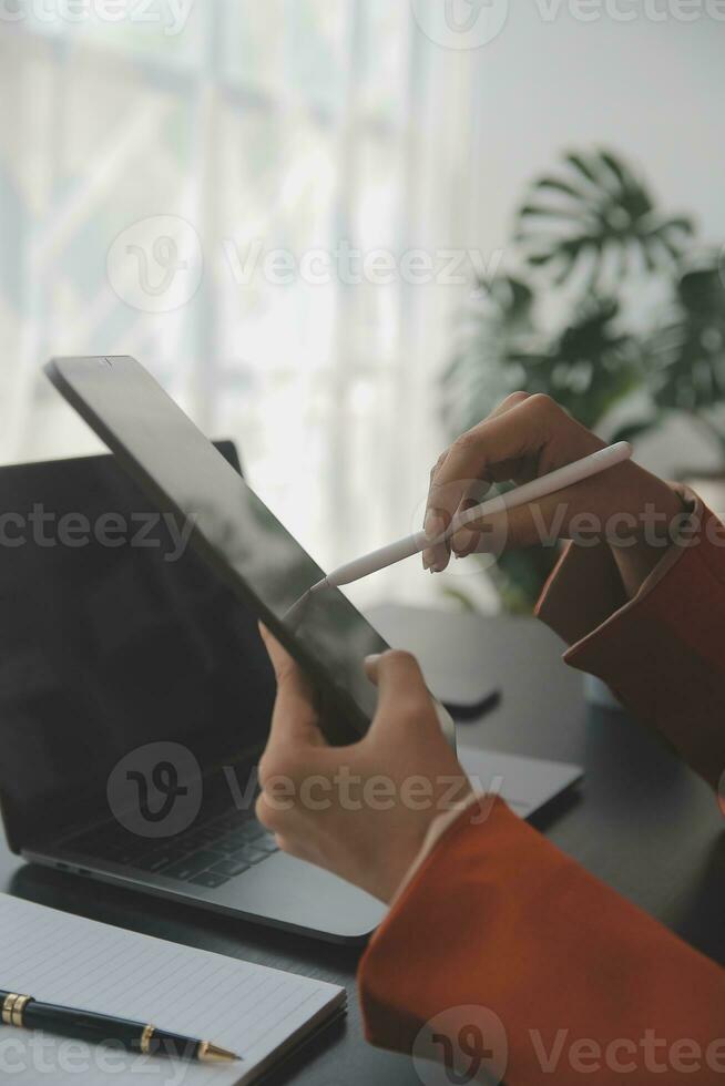 Attractive smiling young asian business woman work at home office, Asian woman working on laptop computer holding tablet. photo