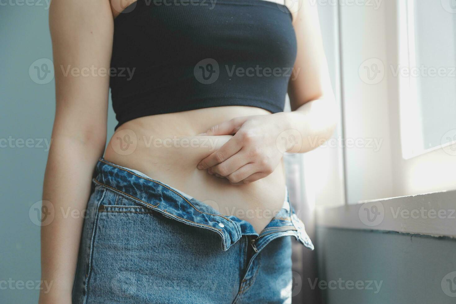 Close up of a belly with scar from c-section and abdominal fat. Women's health. A woman dressed up in sportswear demonstrating her imperfect body after a childbirth with nursery on the background. photo