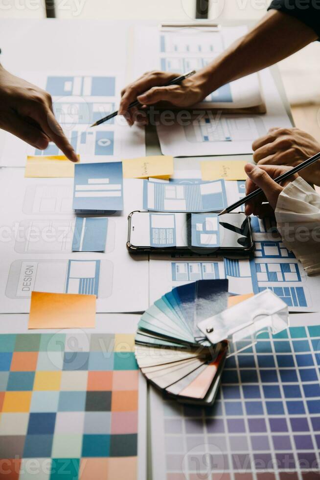 Close up ux developer and ui designer brainstorming about mobile app interface wireframe design on table with customer breif and color code at modern office.Creative digital development agency photo