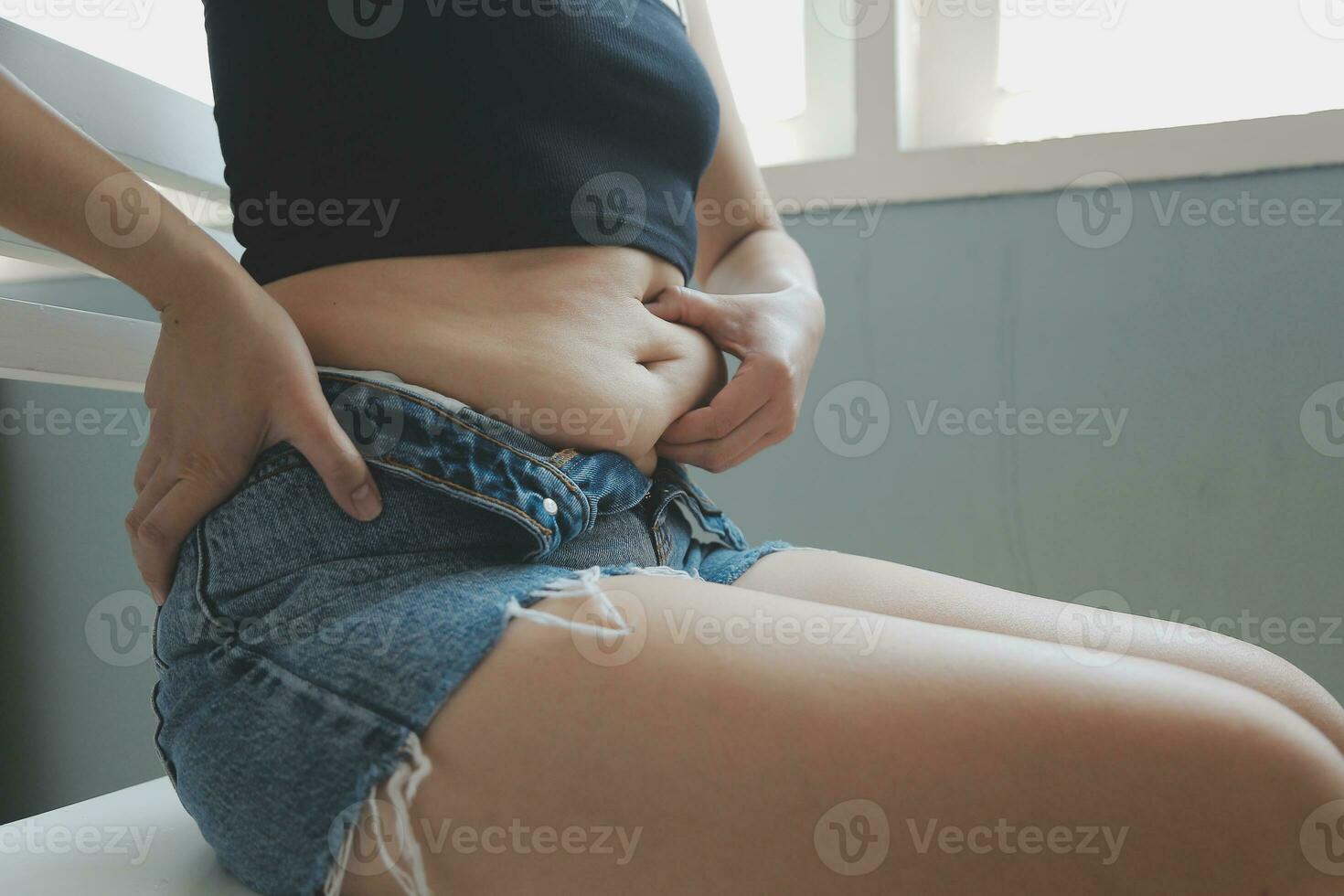 Close up of a belly with scar from c-section and abdominal fat. Women's health. A woman dressed up in sportswear demonstrating her imperfect body after a childbirth with nursery on the background. photo