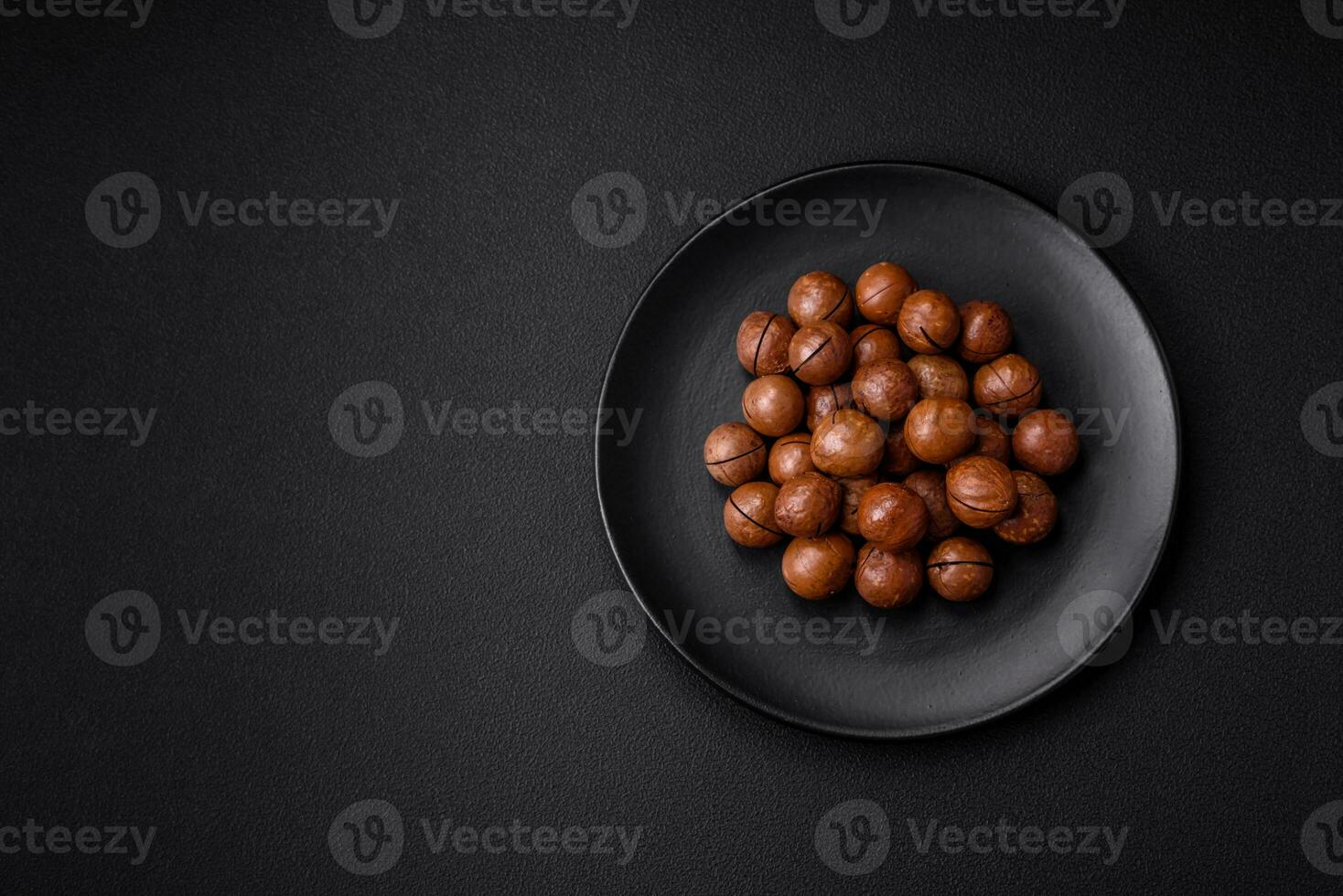 delicioso asado macadamia nueces en cáscara en un oscuro texturizado antecedentes foto