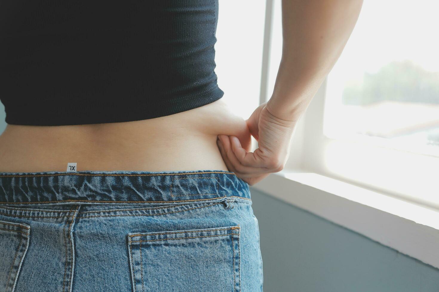 Close up of a belly with scar from c-section and abdominal fat. Women's health. A woman dressed up in sportswear demonstrating her imperfect body after a childbirth with nursery on the background. photo