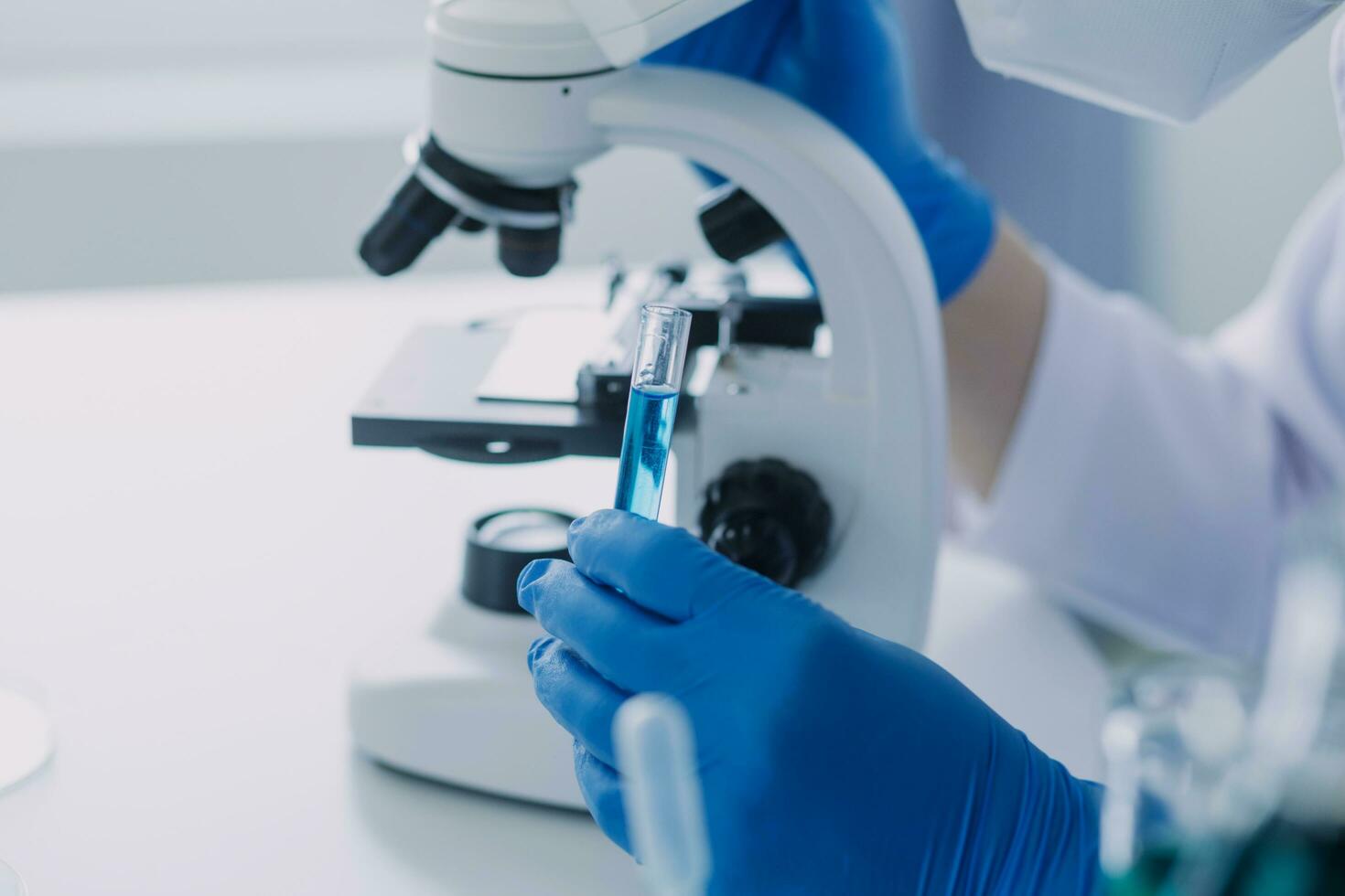 medical or scientific researcher researching and experimenting Multi-colored solution, vial and microscope In the laboratory or in the laboratory by wearing blue gloves and white clothing completely. photo