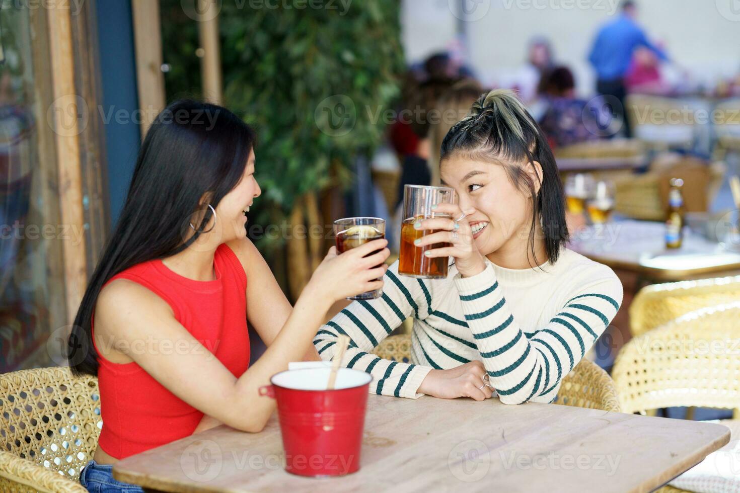 Cheerful Asian friends clinking glasses of drinks in cafe photo