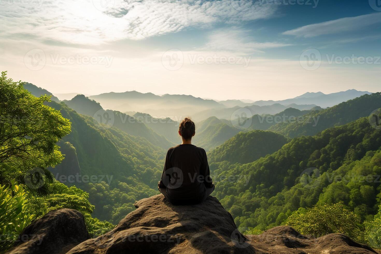 A person meditating on top of a hill, overlooking a vast landscape of mountains and forest. photo