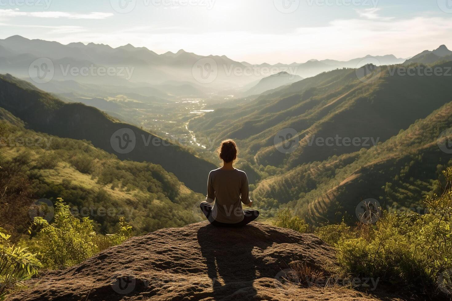 A person meditating on top of a hill, overlooking a vast landscape of mountains and forest. photo