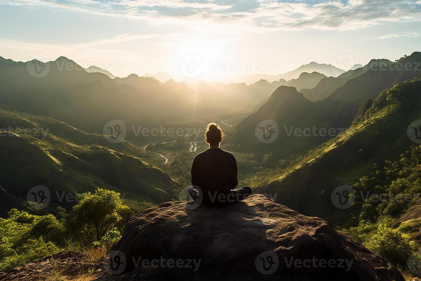 A person meditating on top of a hill, overlooking a vast landscape of mountains and forest. photo