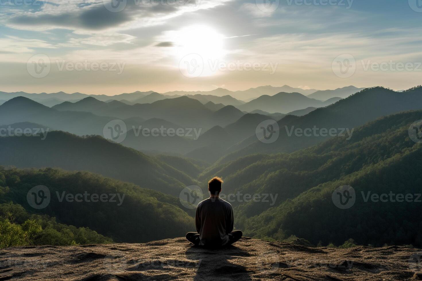 A person meditating on top of a hill, overlooking a vast landscape of mountains and forest. photo