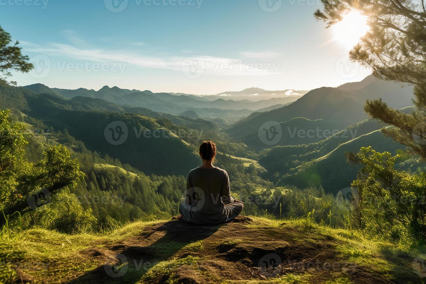 A person meditating on top of a hill, overlooking a vast landscape of mountains and forest. photo