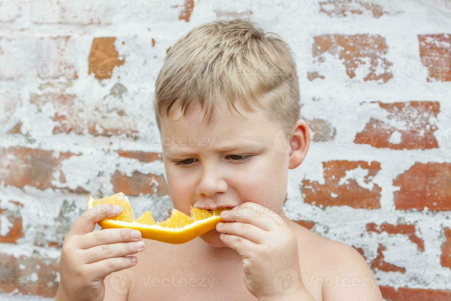 Portrait of child. Cute boy posing and eating a delicious orange. The emotions of a child. photo