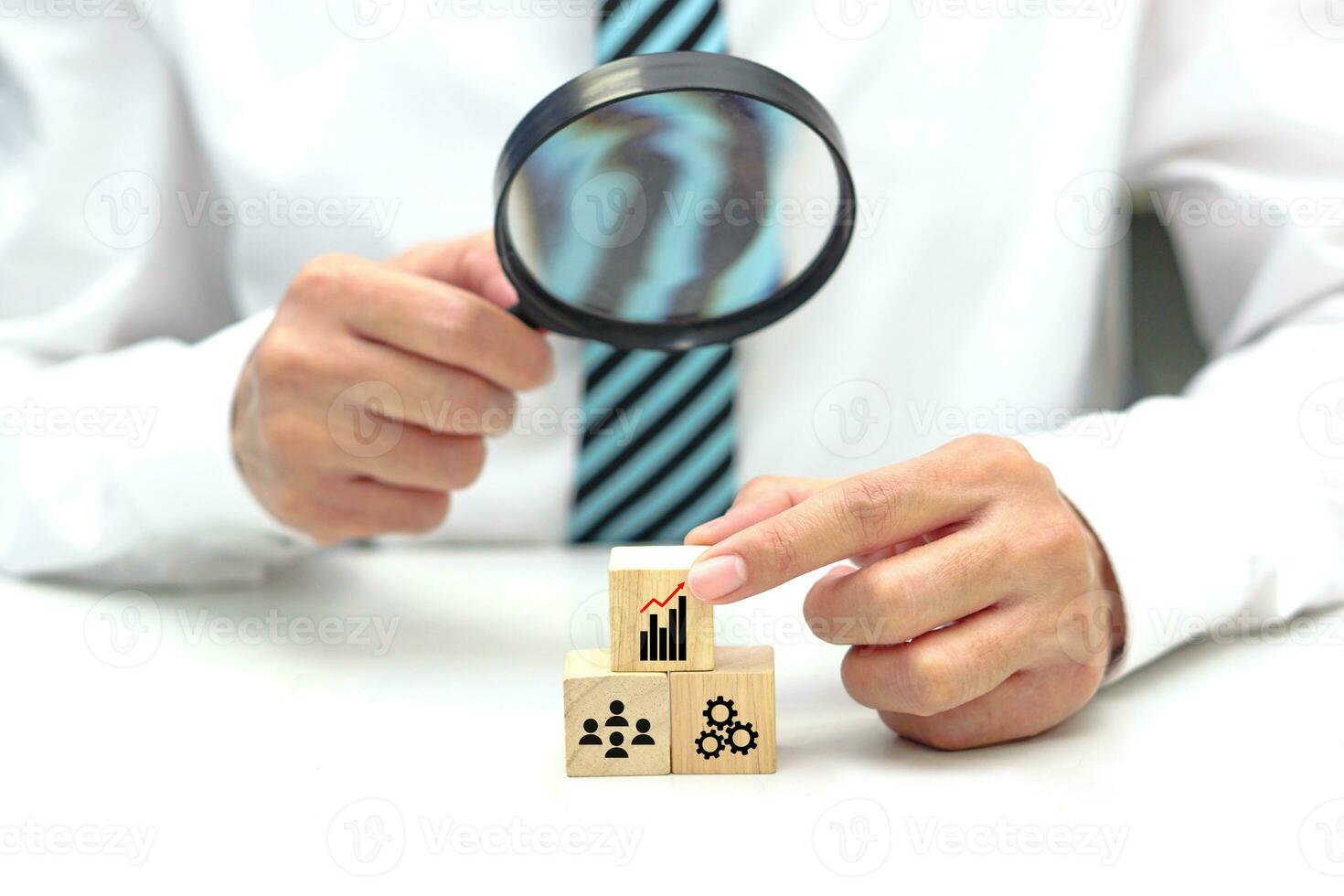 Hand of businessperson looking at wooden blocks with various icon symbols through magnifying glass. Concept of business strategy, goal to increase and action plan. photo