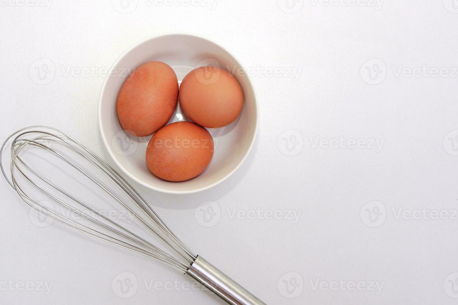 Top view of chickken eggs in a bowl and egg whisks on white background. Copy space. photo
