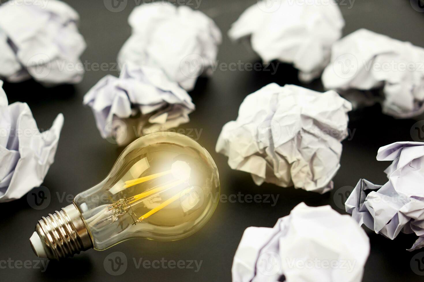 Light bulbs glows orange and crumpled paper on black background. Good idea, creativity and inspiration concept. photo