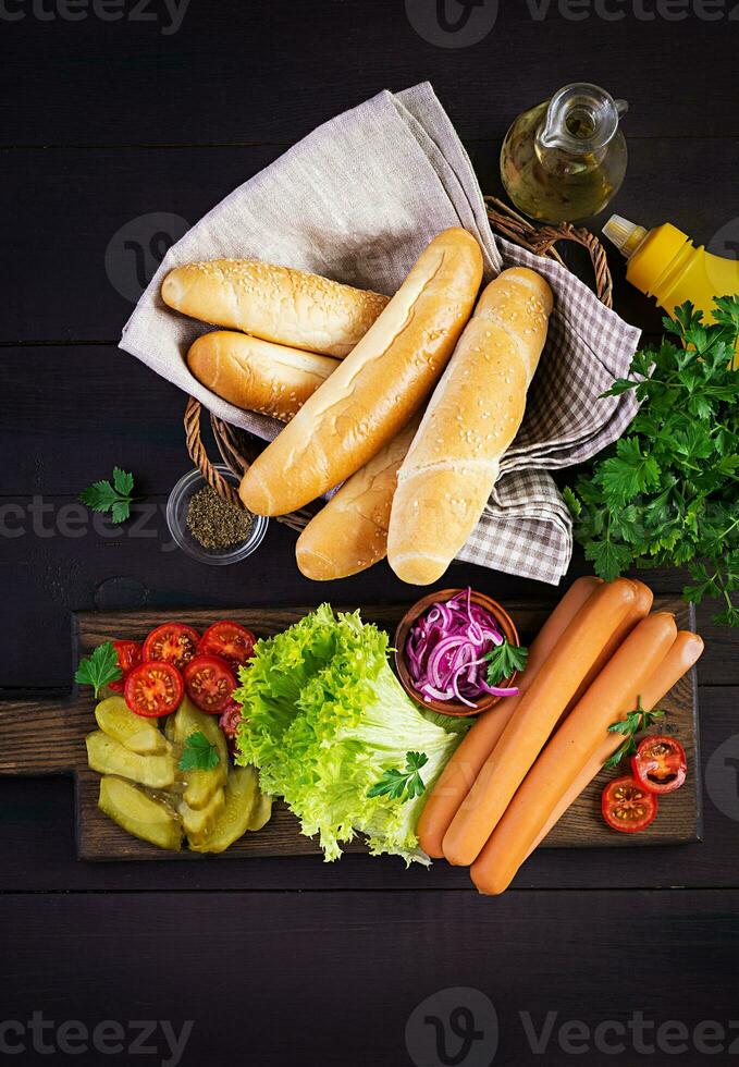 Ingredients for hot dog with  sausage, pickled cucumber, tomatoes, red onions and lettuce on dark wooden background. Summer hotdog. Top view photo