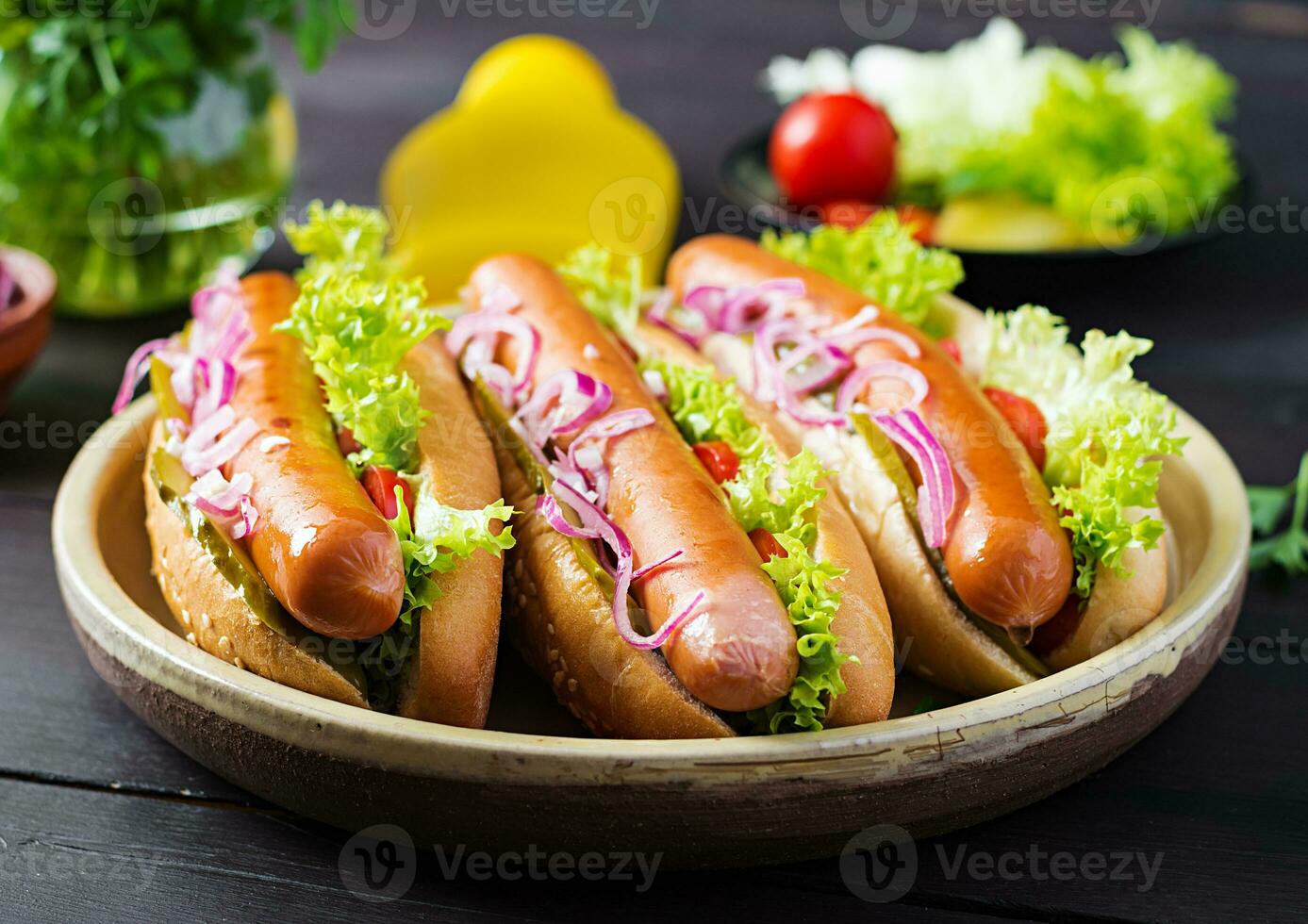 caliente perro con embutido, en escabeche pepino, Tomates, rojo cebollas y lechuga en oscuro de madera antecedentes. verano Hot dog. foto
