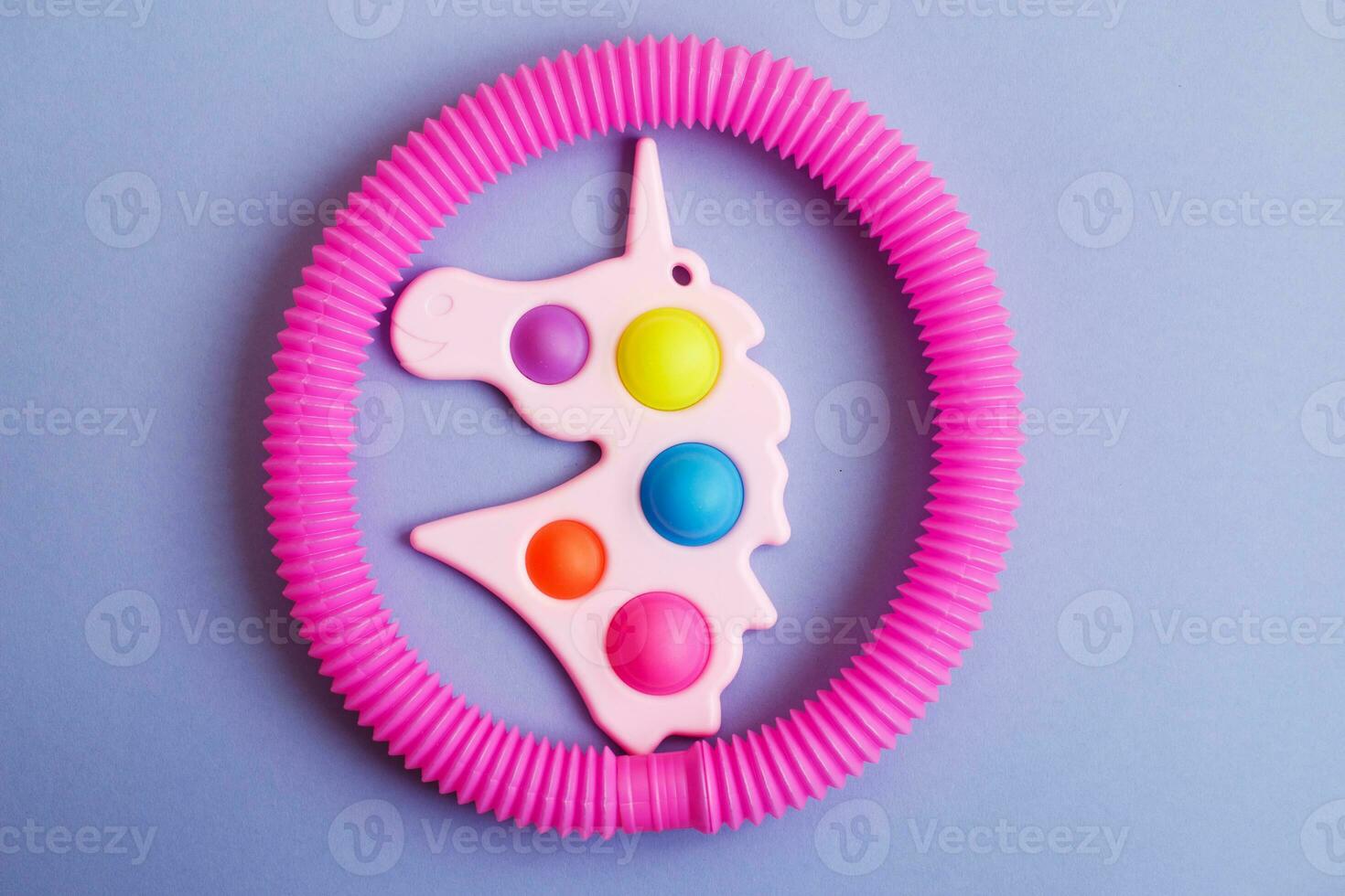 Simple dimple in the form of unicorn and a tube fidget toy on a purple background photo