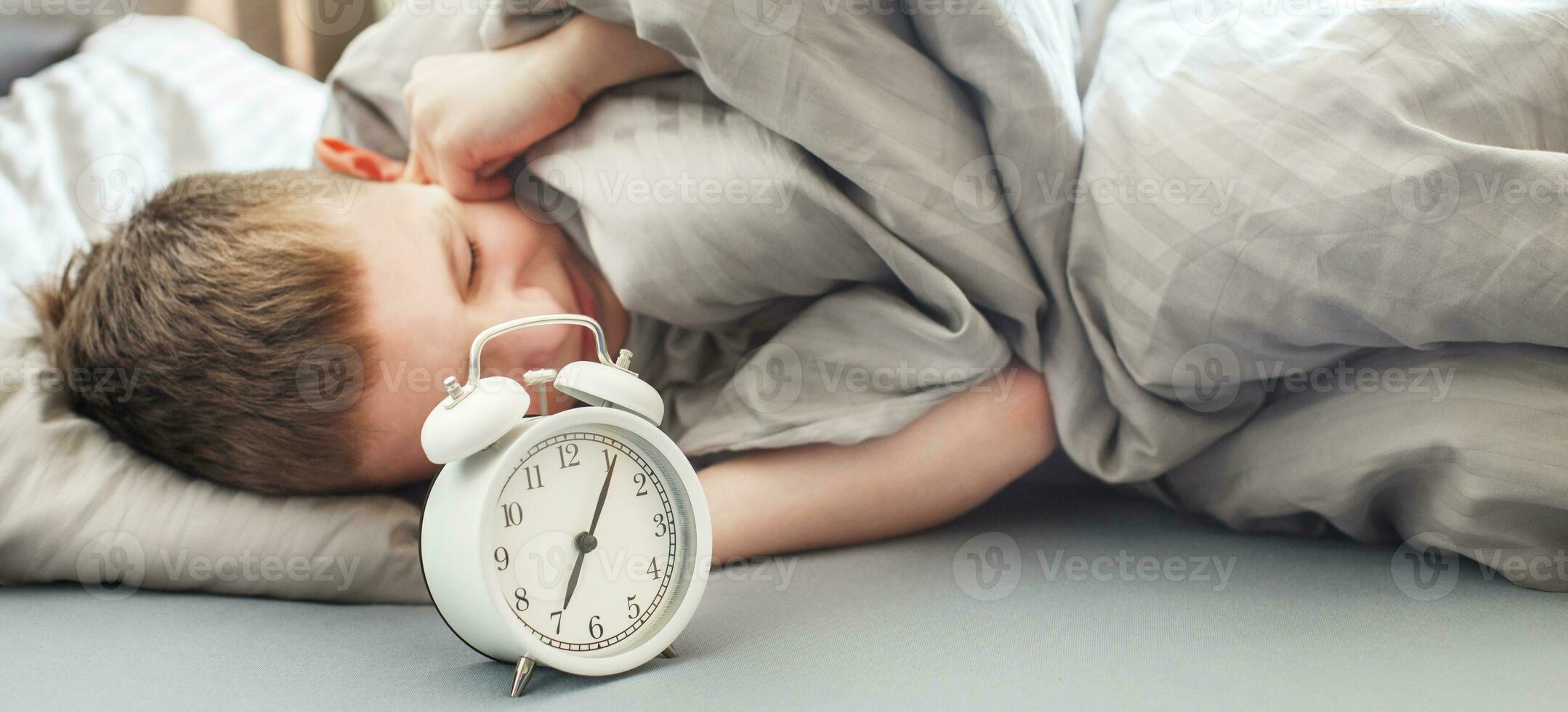 the boy lies on the bed in morning and covers his ears so as not to hear the alarm clock. child does not want to wake up photo