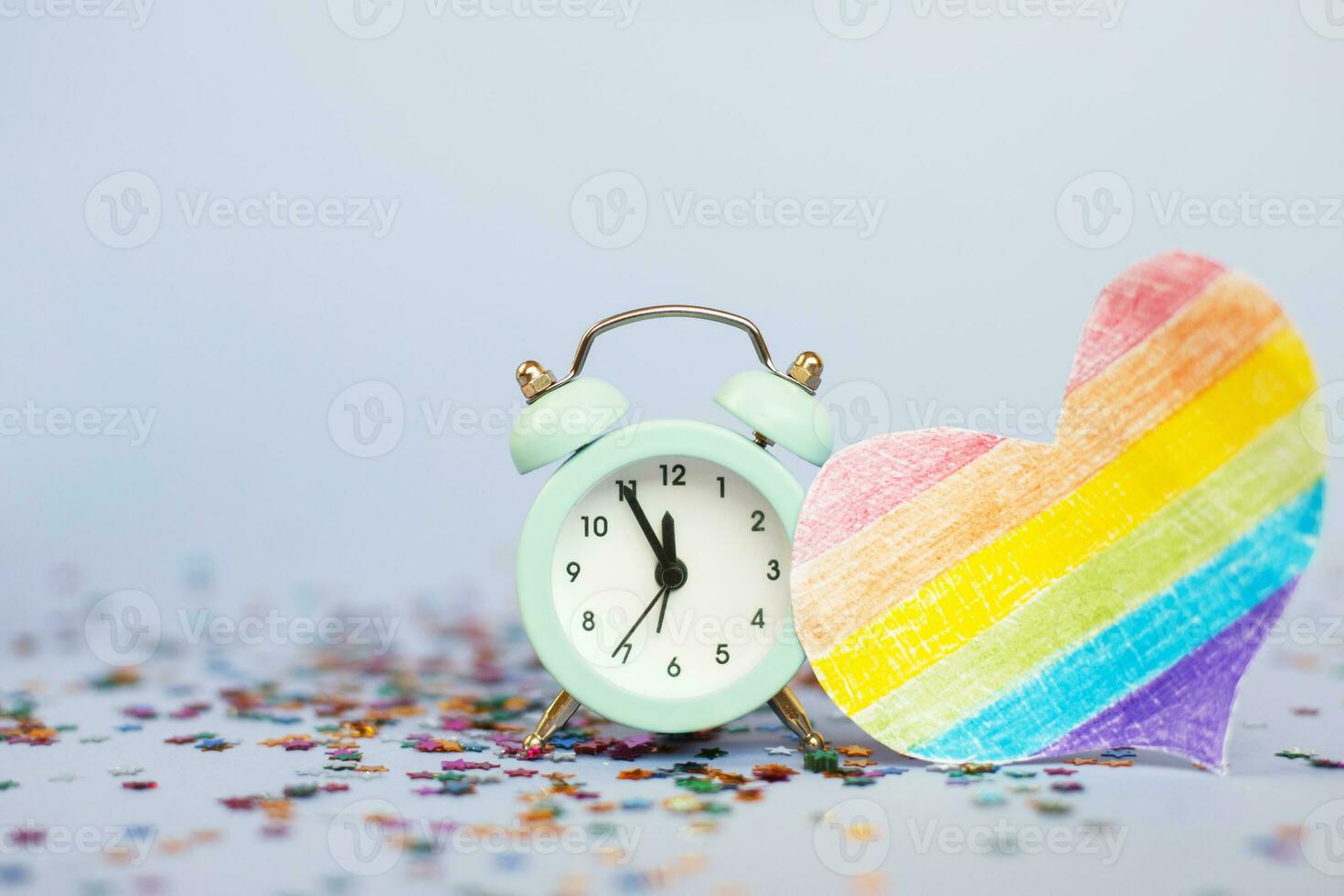 Alarm clock showing five minutes to twelve with milticolored sequins and lgtb flag in the form of a heart photo